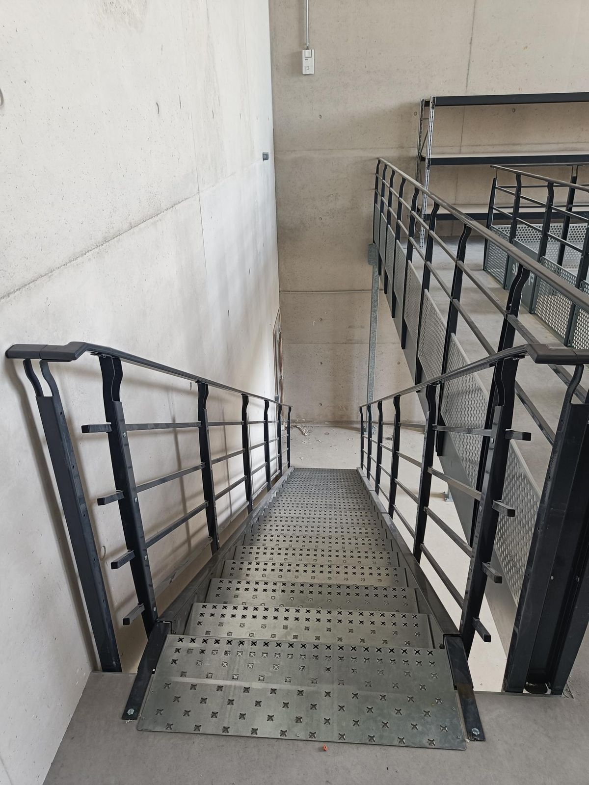 Blick von oben auf eine Lagerbühnen-Treppe mit verzinkten Gitterroststufen und schwarzem Geländer