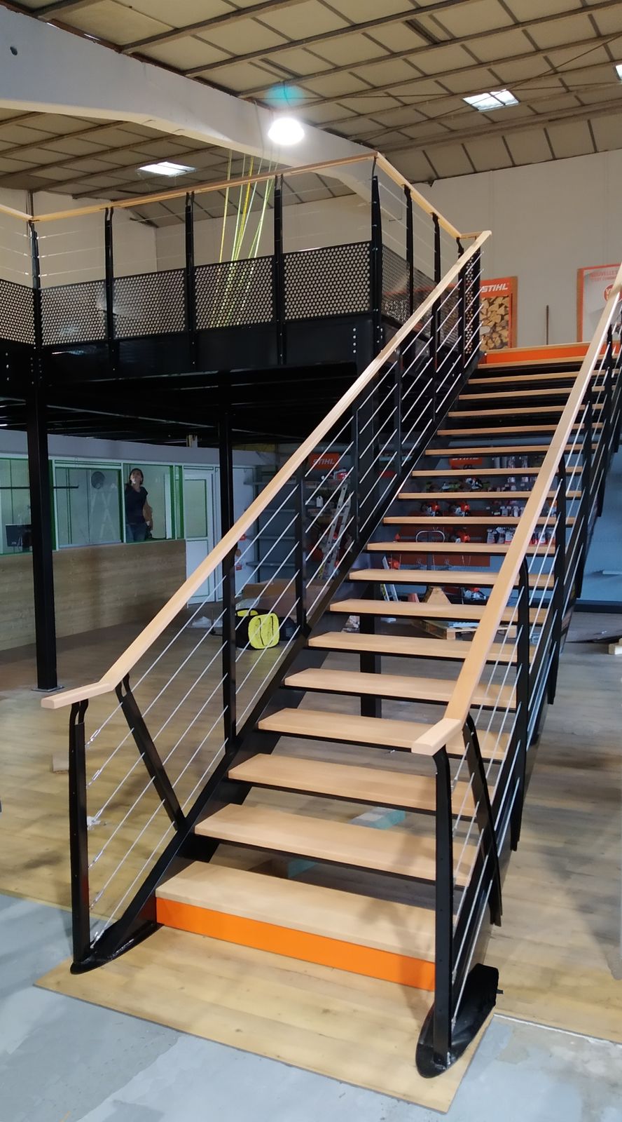 Treppe einer Lagerbühne mit Holzstufen, Holzhandlauf, Seilgeländer und orangefarbener Stufenmarkierung